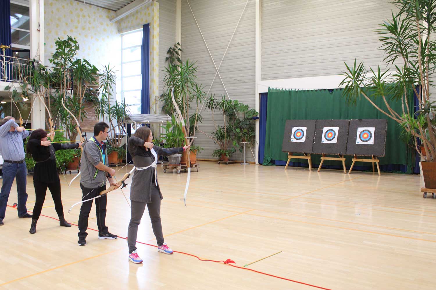 Ein Mann und eine Frau üben in einer Turnhalle das Bogenschießen auf eine Zielscheibe