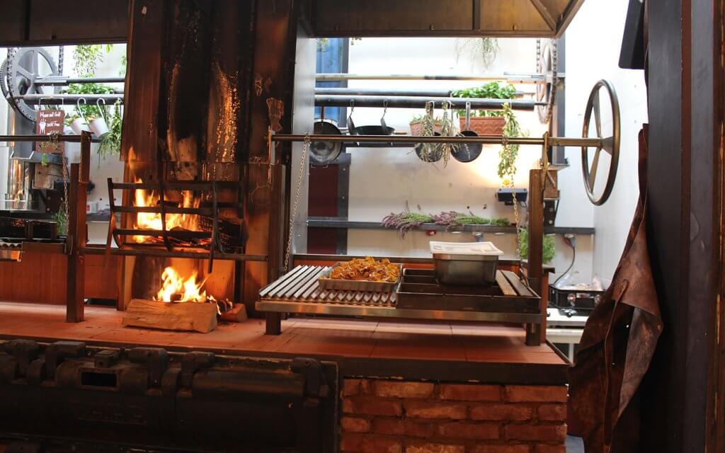 Offene Restaurantküche, Ofen mit brennendem Holzfeuer, schwarze Pfannen an der Wand.